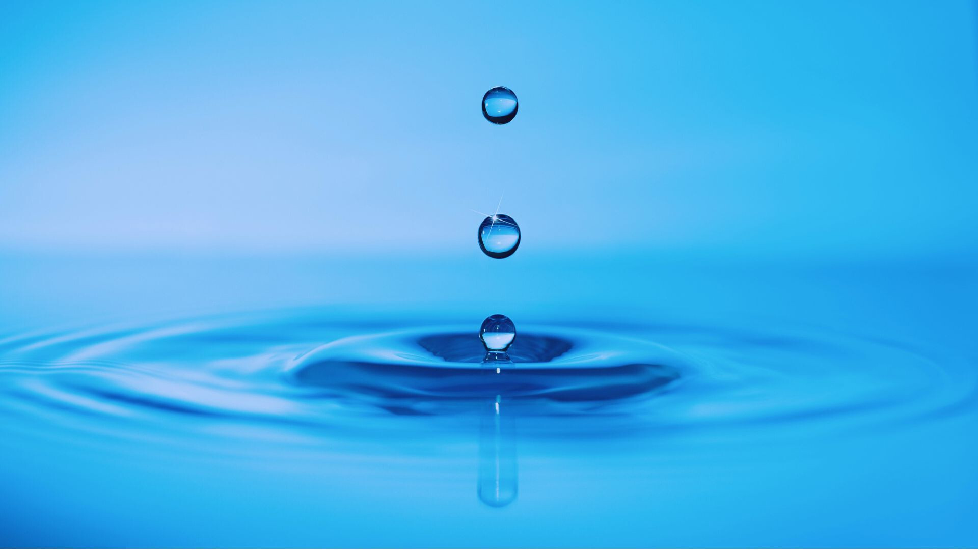 Einzelne Wassertropfen fallen auf eine glatte Wasseroberfläche.